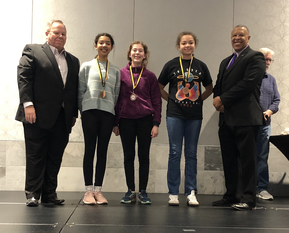  students stand on stage with medals